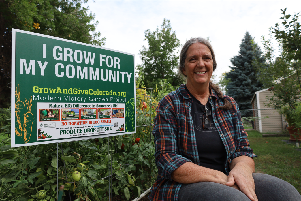 Woman in her garden next to sign that reads I Grow for My Community
