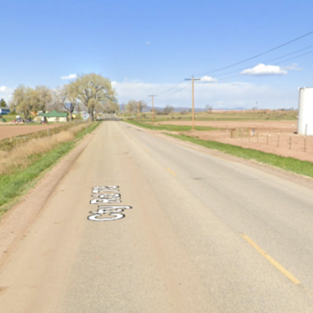 Owl Canyon Road passing by a farm, with a clear blue sky and a few white clouds in the background
