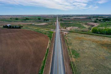 A scenic view of a road stretching through green fields under a clear blue sky with a few white clouds