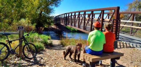 Une famille se reposant sur un banc près d’un pont sur le sentier de la rivière Poudre