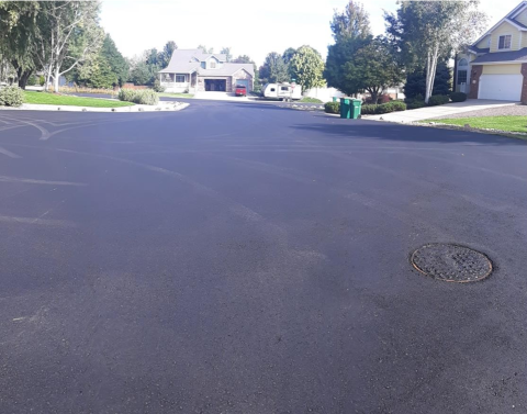 Photo of a freshly paved road in an improvement district neighborhood. Trees and houses line both sides of the street.