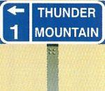 A trail blazer sign featuring a location name, a directional arrow, and the distance to the destination.