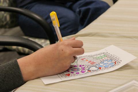 Picture of a hand using a yellow gel pen to color a coloring page with hearts on it