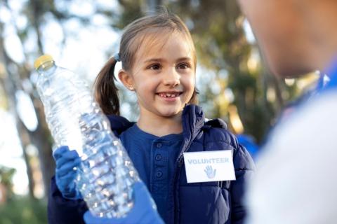 Young girl participating in a recycling program, holding an empty plastic water bottle.