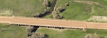 Aerial view of a bridge crossing a creek, surrounded by lush green vegetation.