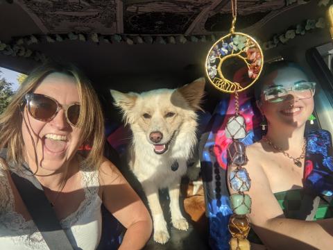 Two women and a dog, seated between them, smile for a photo.