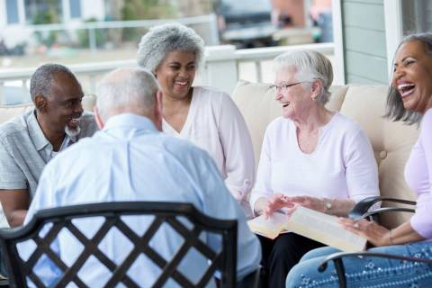 A friend group of older adults seated and chatting on an outdoor patio