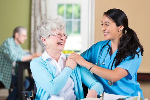 An older adult laughs during a conversation with a caring profession as the two clasp hands