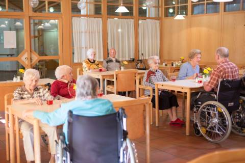 Care community residents have tea at wooden tables in a dining room