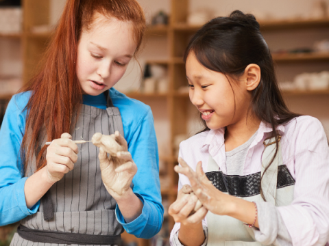 Two children build a figure out of clay