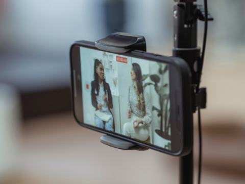 An image of a phone screen. The phone is on a tripod. Two teens are being video taped by the phone.