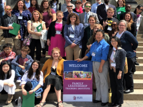 A large group stands on steps - holding an FLTI sign.