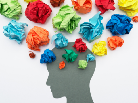 A silhouette of a head. Crumpled balls of multiple colored paper hover over the head.