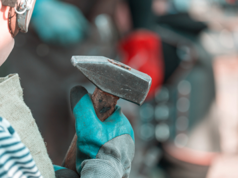 A pre-teen holds a hammer preparing to strike it on an anvil