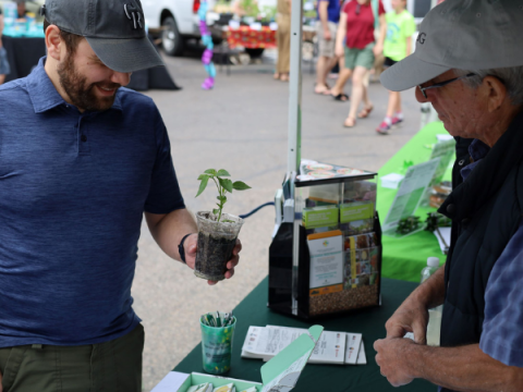 लैरिमर काउंटी फार्मर्स मार्केट में एक वयस्क पुरुष एक मास्टर माली के साथ एक पौधे के बारे में बात करता है