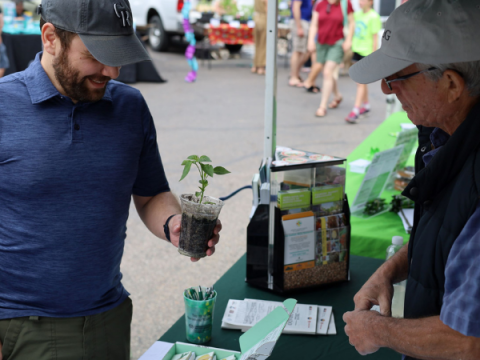 En vuxen hane pratar om en växt med en trädgårdsmästare på Larimer County Farmers' Market