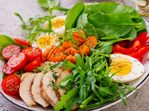 A healthy looking salad with mixed greens, a boiled egg, tomatoes, pepper, etc.