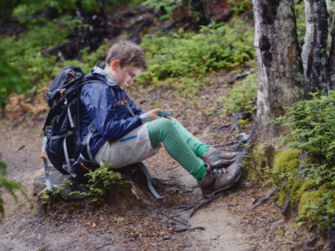 A teenager sits by a trail wearing hiking gear