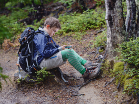 Ein Teenager sitzt mit Wanderausrüstung an einem Wanderweg