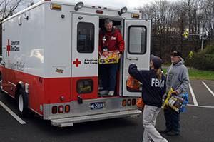 Person unloading a box from the back of a Red Cross truck and handing the box to FEMA staff