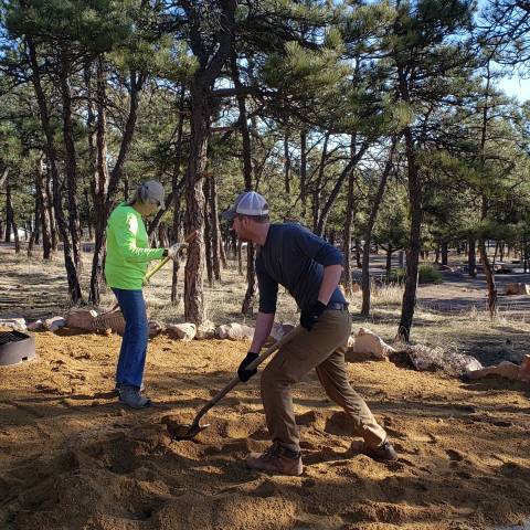 Zwei Freiwillige harken und schaufeln Sand auf dem Campingplatz.