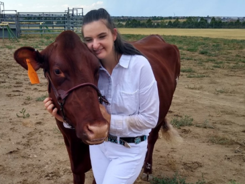 A young woman wearing white stands next to her dairy cow.