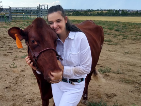 Una mujer joven vestida de blanco se para al lado de su vaca lechera.